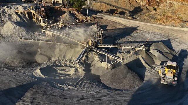 Yellow loader moving gravel piles at a busy industrial stone processing facility