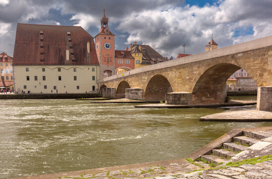 Historic riverside buildings and clock tower beside the Stone Bridge on the Danube River in Regensburg, Bavaria, Germany.