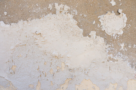 Textured wall with peeling white paint and a sandy background. The surface shows signs of wear and age, creating an abstract pattern.