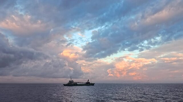 Versatile real-time wide angle video of workboat with crane sailing under dramatic glowing sunset clouds for video background
