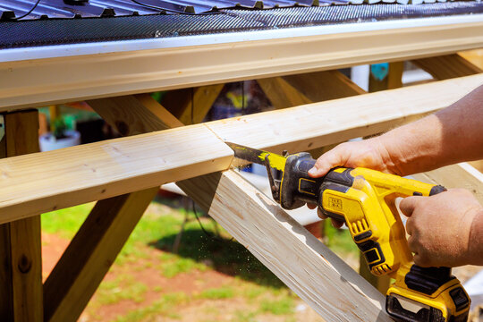 Worker cuts wood with power tool while working on structure outside