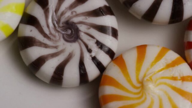 Colorful swirled peppermint candies rotating slowly on white background
