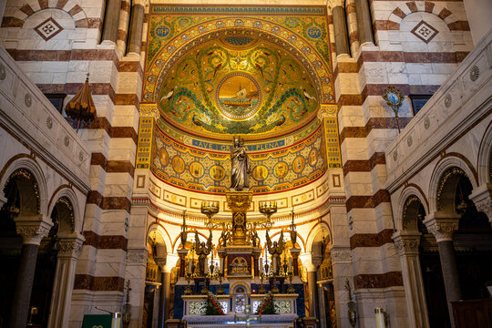 Ornate altar and richly decorated apse inside Notre-Dame de la Garde Basilica in Marseille, France. Golden mosaics, colorful religious artwork and a statue of the Virgin Mary highlight the sanctuary.