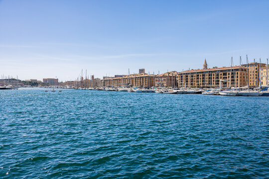 Panoramic view of sailboats and leisure vessels moored at the Old Port of Marseille, France. Historic waterfront buildings line the vibrant Mediterranean harbor beneath a clear blue sky