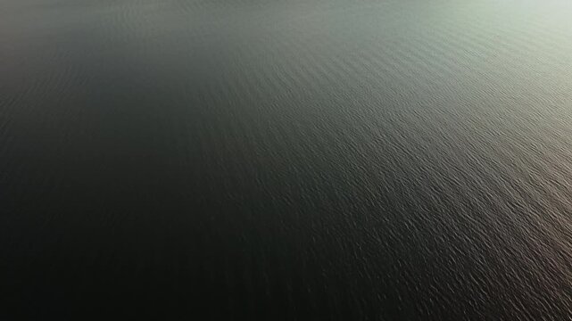 Aerial drone view over calm, dark water on Batak Reservoir in Bulgaria with subtle ripples and moody light