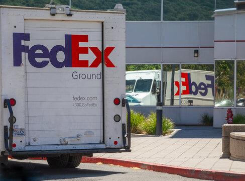 FedEx Ground delivery truck parked near commercial building with branded rear door and reflective windows showing mirrored logo