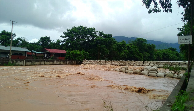 豪雨により激しく増水・濁流化した川と積まれた浸水対策の土嚢袋
