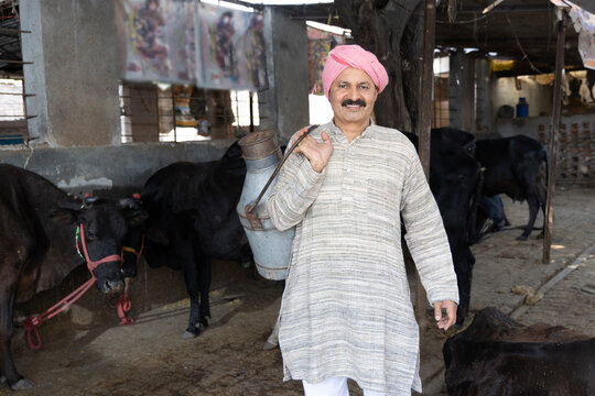 Happy Indian farmer showing milk cane and selling milk in farm - concept of milk production Agri business, rural India, growth and agriculture. Milkman collecting milk at dairy farm