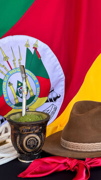 Chimarr&atilde;o, gaucho hat and scarf on the table, and the flag of the state of Rio Grande do Sul - Brazil  in the background. Farroupilha Week.