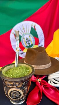 Chimarr&atilde;o, gaucho hat and scarf on the table, and the flag of the state of Rio Grande do Sul - Brazil  in the background. Farroupilha Week.