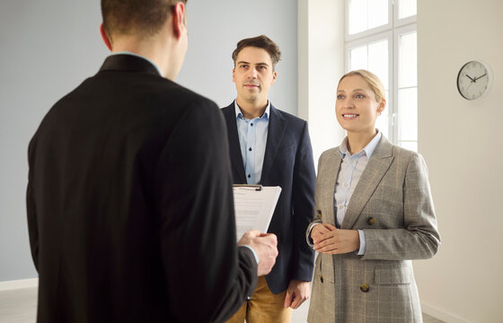 Realtor meets couple clients for apartment viewing. Clients talk with the agent in a bright empty room during a property meeting and tour, reviewing options. Clear concept of home purchase.