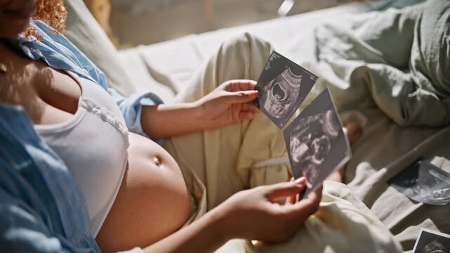 Future mom examining sonogram scans home bedroom. Closeup happy pregnant belly.
