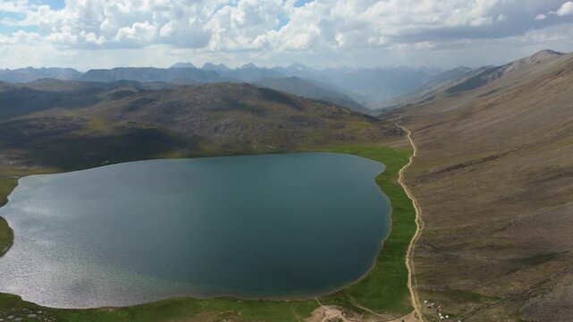 left to right aerial pan revealing the turquoise waters of high altitude Lake in Deosai National Park, with dramatic cloud shadows moving across the rolling green mountains