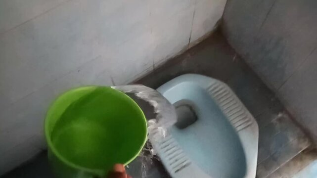 Person manually flushing a toilet using a water dipper, illustrating traditional bathroom cleaning, household sanitation, and everyday hygiene practices in Indonesia.