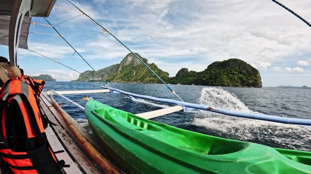 Kayaks and life jackets are positioned on a boat as it moves through the clear waters near tropical islands, showcasing beautiful rock formations