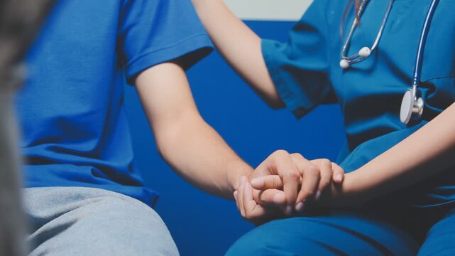 Doctor holding patient's hand on a white desk during medical consultation, offering support, empathy, care, reassurance, and compassion in a hospital or clinic setting