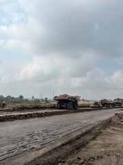 Rear angle view of heavy dump trucks carrying overburden material on dirt haul road at open mine © faaqiihh