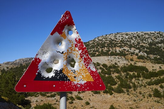 A damaged road sign with bullet holes in front of a mountainous landscape and blue sky, Lefka Ori, White Mountains, mountain massif, west, Crete, Greece
