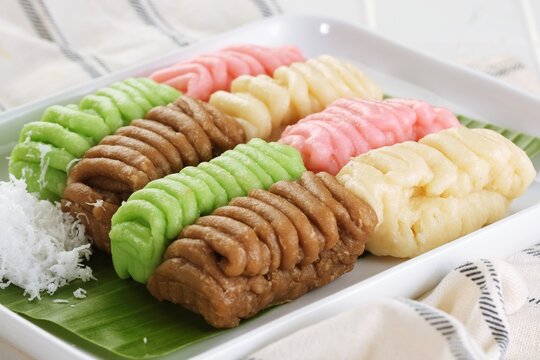 Traditional getuk lindri made from mashed cassava, arranged in colorful rows with grated coconut and banana leaf on a white plate for an Indonesian food concept.