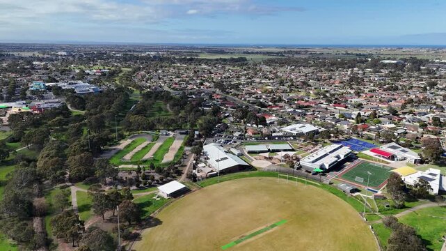 Aerial view over a suburban sports oval, school facilities, and a BMX track, surrounded by suburban houses in a residential neighbourhood, Werribee, Melbourne, Australia