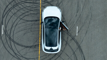 Woman stands near ev car. She poses by white ev car. Stylish ev car on road. © Nutchanart