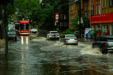 A streetcar and vehicles navigate a flooded commercial street lined with brick buildings after a heavy rainstorm