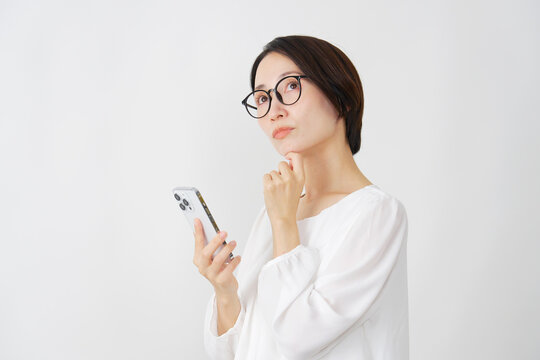 スマホを持って考えるミドル女性　白背景