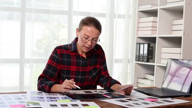 Young creative UX designer working on a mobile app wireframe, developing a new user interface and selecting a color scheme on a digital tablet in a modern office