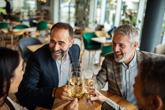 Mature friends toasting wine in modern restaurant