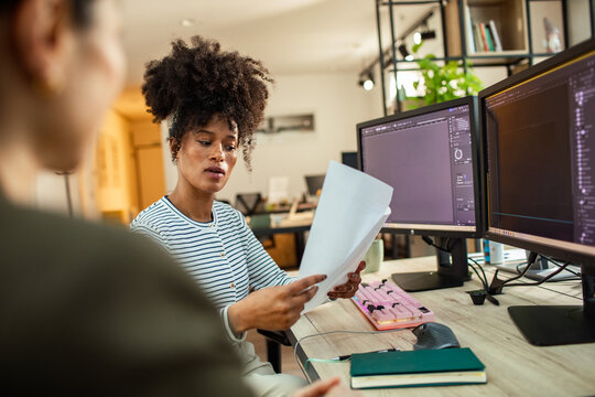 Designer reviewing project documents at dual monitors in modern office