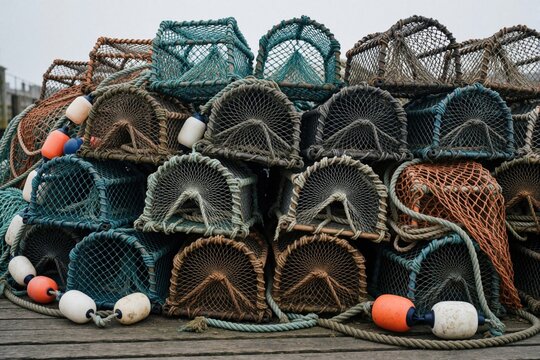 Heap of commercial crab pots, fishing nets on wooden quayside. Large pile of stacked lobster traps with ropes, colorful plastic floats. Maritime equipment for seafood industry lies outdoors near sea