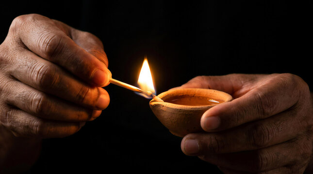 Close up of senior hands lighting traditional earthen clay oil lamp with burning match in the dark