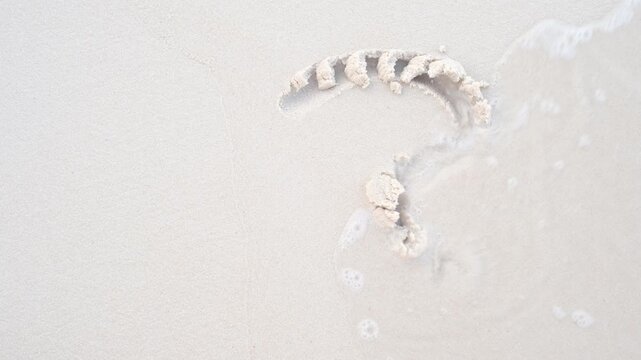 A woman's hand draws question mark on sand, top view.