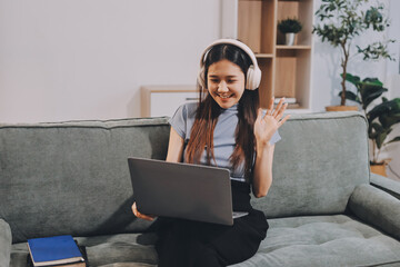 Beautiful young asian woman sitting on sofa and holding joystick playing online video game in living room at house © ARMMY PICCA