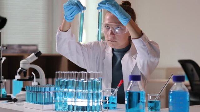 Female scientist working with test tubes and blue liquid in a laboratory for research and development, analyzing a chemical sample while developing a new vaccine or treatment