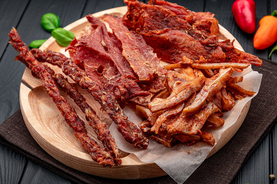 Beef jerky and meat snacks on a wooden platter. Various types of beef jerky and meat snacks are arranged on a round wooden platter.