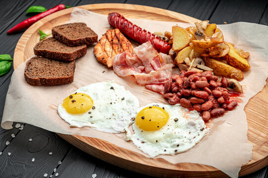 Breakfast platter with eggs, sausage, bacon, beans, and potatoes on a wooden board. Food on a wooden board shows eggs, sausage, bacon, beans, and potatoes at a breakfast table.