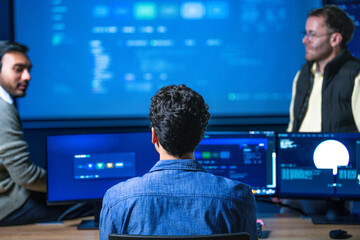 Fototapeta premium An experienced technology manager coaching an analyst at his workstation points at a line on the monitor while the younger engineer listens in a quiet corporate office