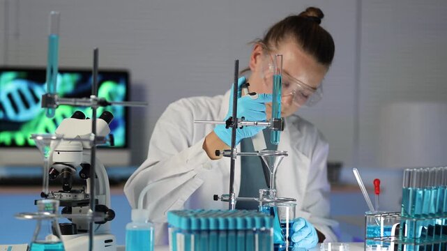 Female scientist conducting titration experiment using a burette and beaker in a modern chemical laboratory with a microscope and DNA helix on a monitor in the background