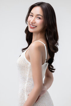 Beauty portrait of a joyful young Asian woman with a radiant smile and dark wavy hair, posing in profile and looking towards the camera.