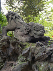 Fototapeta premium Stone Guardian Lion Statue surrounded Green Leaves at Japanese shinto shrine