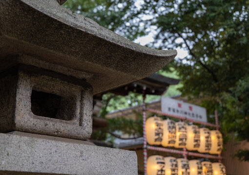 Stone lantern at a traditional Japanese shrine with blurred paper lanterns in the background.