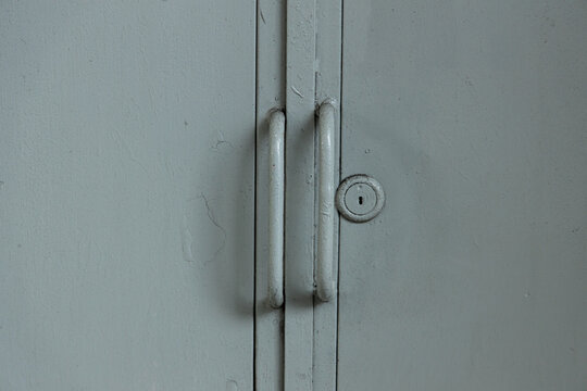 Close view of a gray cabinet door with handles and a keyhole in a simple room