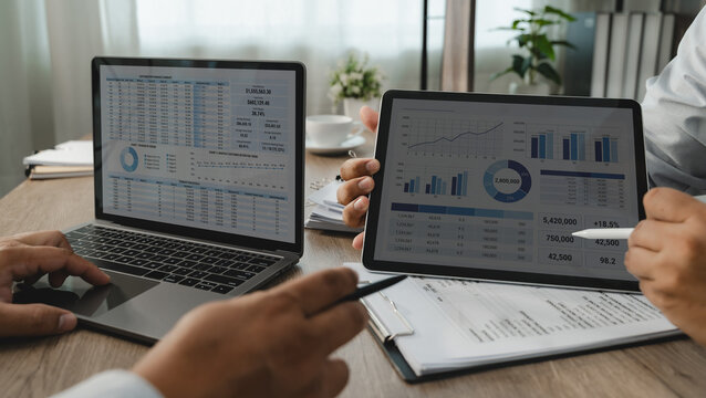 Two businessmen reviewing financial reports on laptop and tablet for accounting analysis, business finance, data comparison and reporting workflow.