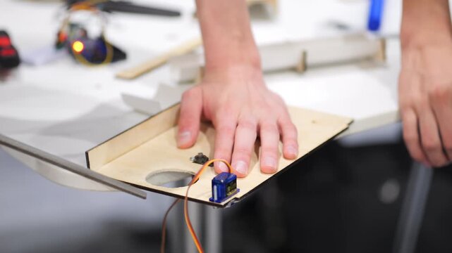 Hands assemble electronic circuit on wooden board. Tools and wires visible. Close-up on crafting process. Focus on DIY electronics project