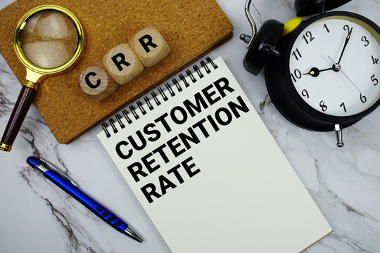 CRR Customer Retention Rate text written on notepad with magnifying glass and alarm clock on marble background