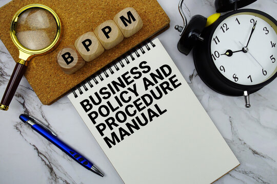 BPPM Business Policy and Procedure Manual text written on notepad with magnifying glass and alarm clock on marble background
