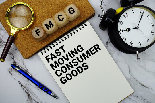 FMCG Fast Moving Consumer Goods text written on notepad with magnifying glass and alarm clock on marble background