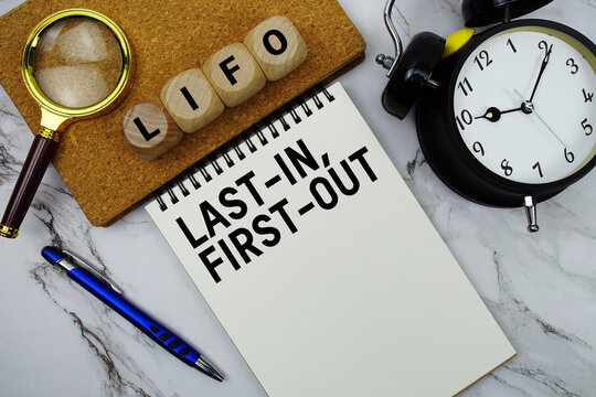 LIFO Last-In, First-Out text written on notepad with magnifying glass and alarm clock on marble background