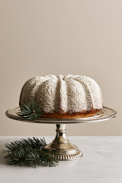 Powdered sugar dusted bundt cake on silver pedestal stand with pine branches, Christmas holiday dessert.